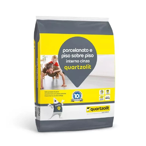 Um saco de 20kg de argamassa 'Piso sobre Piso' da marca Quartzolit na cor cinza. A embalagem é branca e laranja, com informações sobre o produto ser um cimentcola para sobreposição de revestimentos internos. Um saco de 20kg de argamassa 'Piso sobre Piso' da marca Quartzolit na cor cinza. A embalagem é branca e laranja, com informações sobre o produto ser um cimentcola para sobreposição de revestimentos internos.