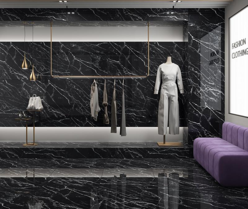 Ambiente moderno e luxuoso com paredes e piso revestidos por porcelanato preto polido, que simula mármore com veios brancos marcantes. O espaço conta com iluminação embutida, araras de metal dourado para roupas, um manequim branco com roupa cinza clara, bolsas em um pedestal e um sofá roxo estofado, indicando ser uma loja de roupas ou showroom.