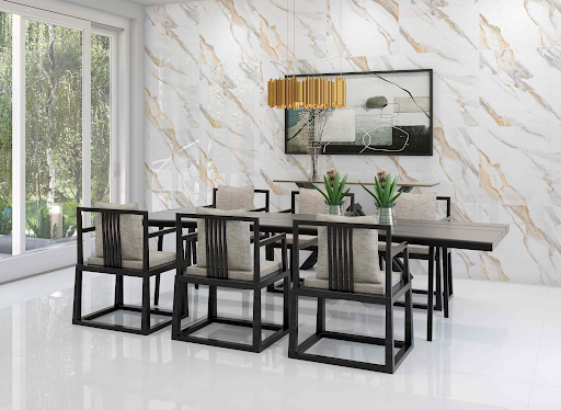 Sala de jantar moderna e luxuosa com mesa preta e seis cadeiras de estrutura escura e estofado bege. O piso é branco de alto brilho e a parede de fundo é revestida com grandes placas marmorizadas brancas com veios dourados e cinzas. Uma luminária pendente dourada está suspensa sobre a mesa e uma grande porta de vidro à esquerda mostra um jardim.