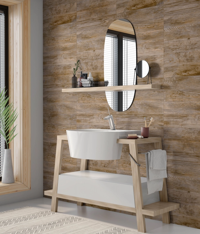 Um banheiro moderno com uma parede de fundo totalmente revestida com cerâmica que imita tábuas de madeira. Possui uma bancada de lavatório com estrutura de madeira clara e cuba branca, um espelho oval sem moldura e uma prateleira de madeira acima da pia. Há uma janela vertical com venezianas à esquerda e plantas decorativas.