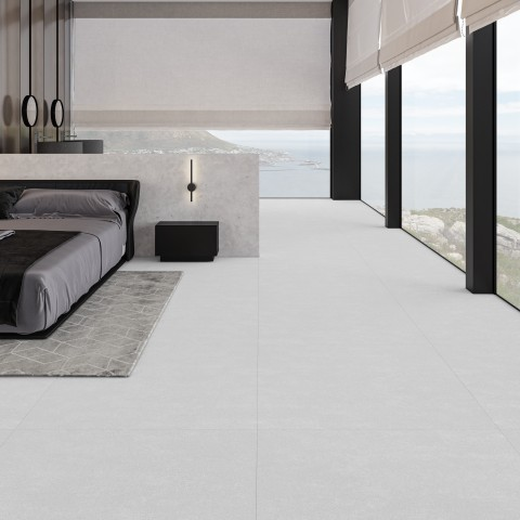 Quarto de casal amplo e minimalista com vista panorâmica para o mar através de grandes janelas de vidro. O piso é revestido com placas grandes de porcelanato cimento queimado cinza-claro em tom suave. À esquerda, uma cama de casal com enxoval em tons de cinza e preto repousa sobre um tapete estampado cinza. Ao fundo, uma divisória meia-parede separa a área de dormir do banheiro integrado. Quarto de casal amplo e minimalista com vista panorâmica para o mar através de grandes janelas de vidro. O piso é revestido com placas grandes de porcelanato cimento queimado cinza-claro em tom suave. À esquerda, uma cama de casal com enxoval em tons de cinza e preto repousa sobre um tapete estampado cinza. Ao fundo, uma divisória meia-parede separa a área de dormir do banheiro integrado.