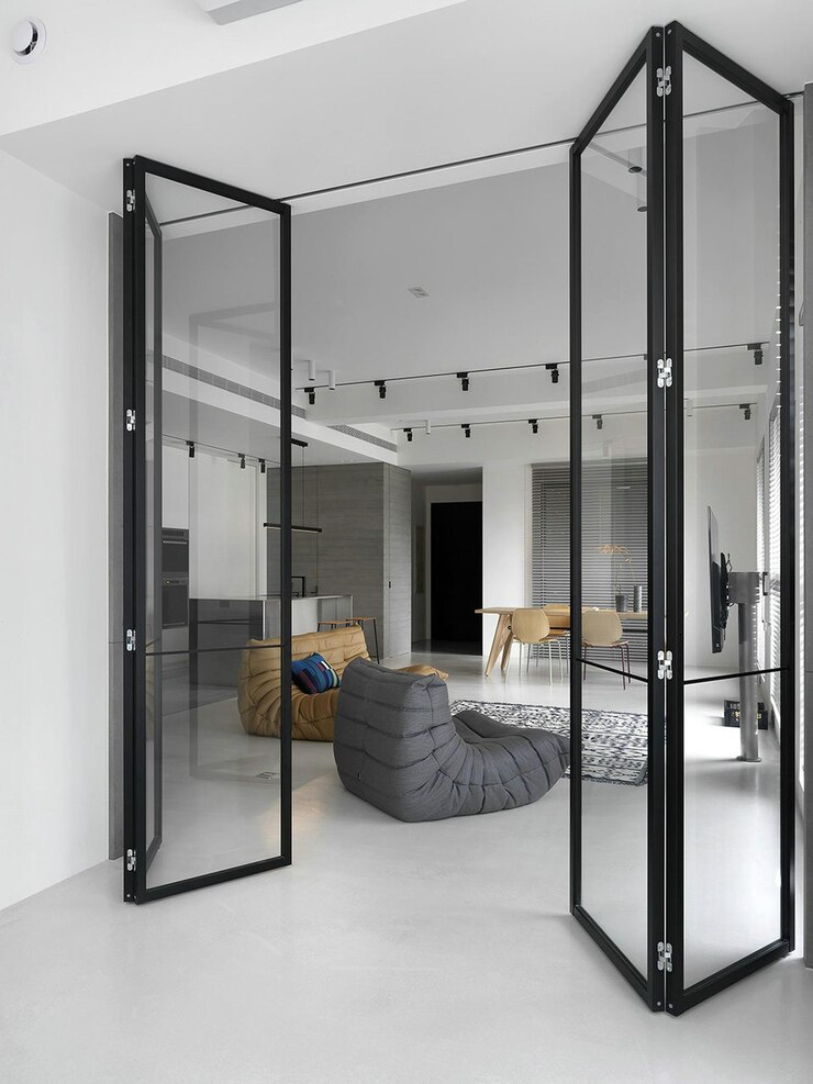 Porta camarão de vidro com estrutura preta, parcialmente aberta, conectando dois ambientes internos de uma casa moderna.