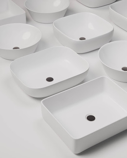  Texto alternativo: Uma vista de cima (flat lay) de várias cubas de apoio brancas, em diferentes formatos, incluindo oval, quadrada e retangular. As cubas têm um ralo preto no centro e estão dispostas em um fundo branco, destacando a variedade de design e tamanho.